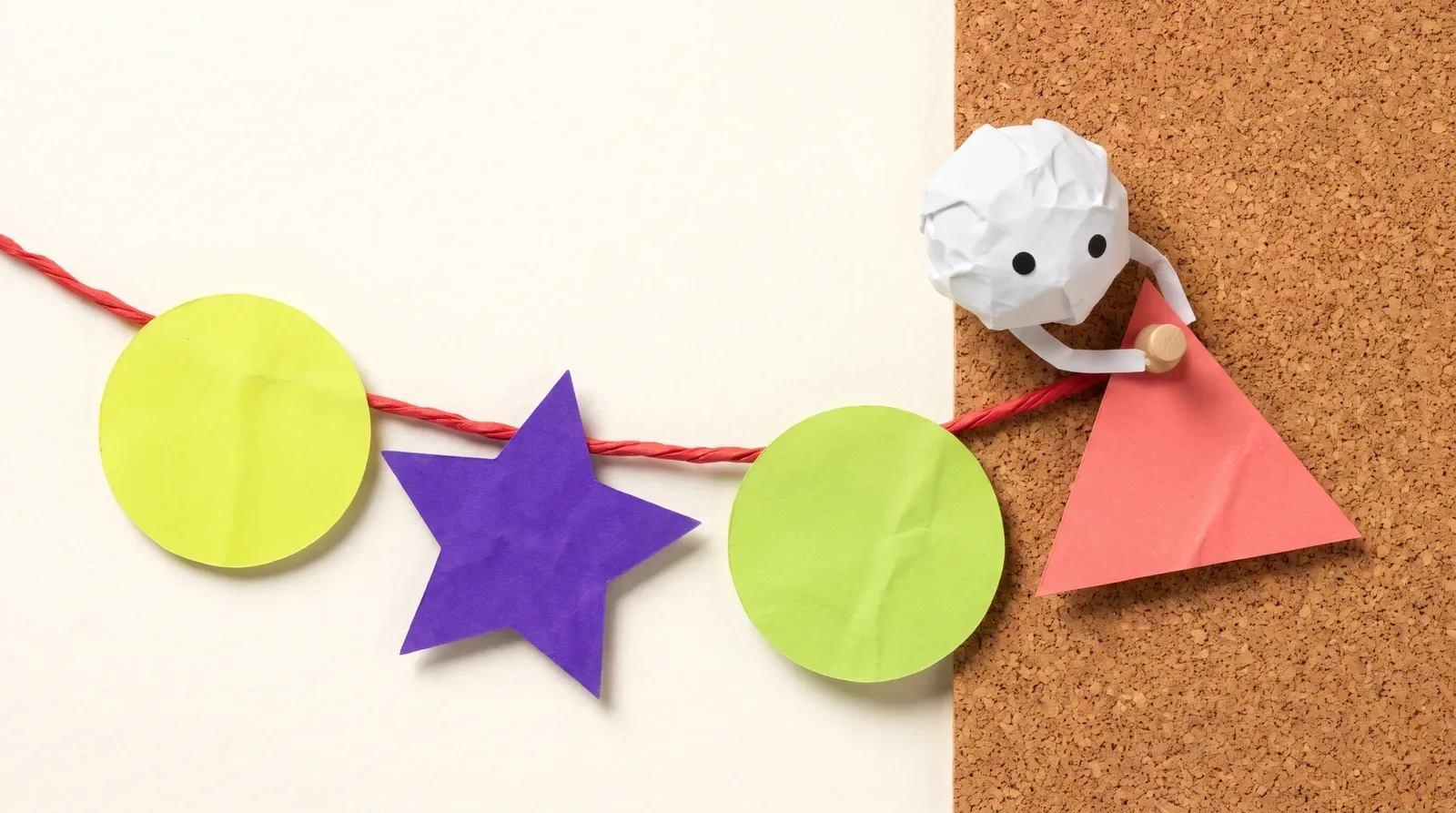 Pip the paper ball hanging a circle, a star, a circle and a triangle on a red string by a cork board, like a song's verse, chorus and bridge